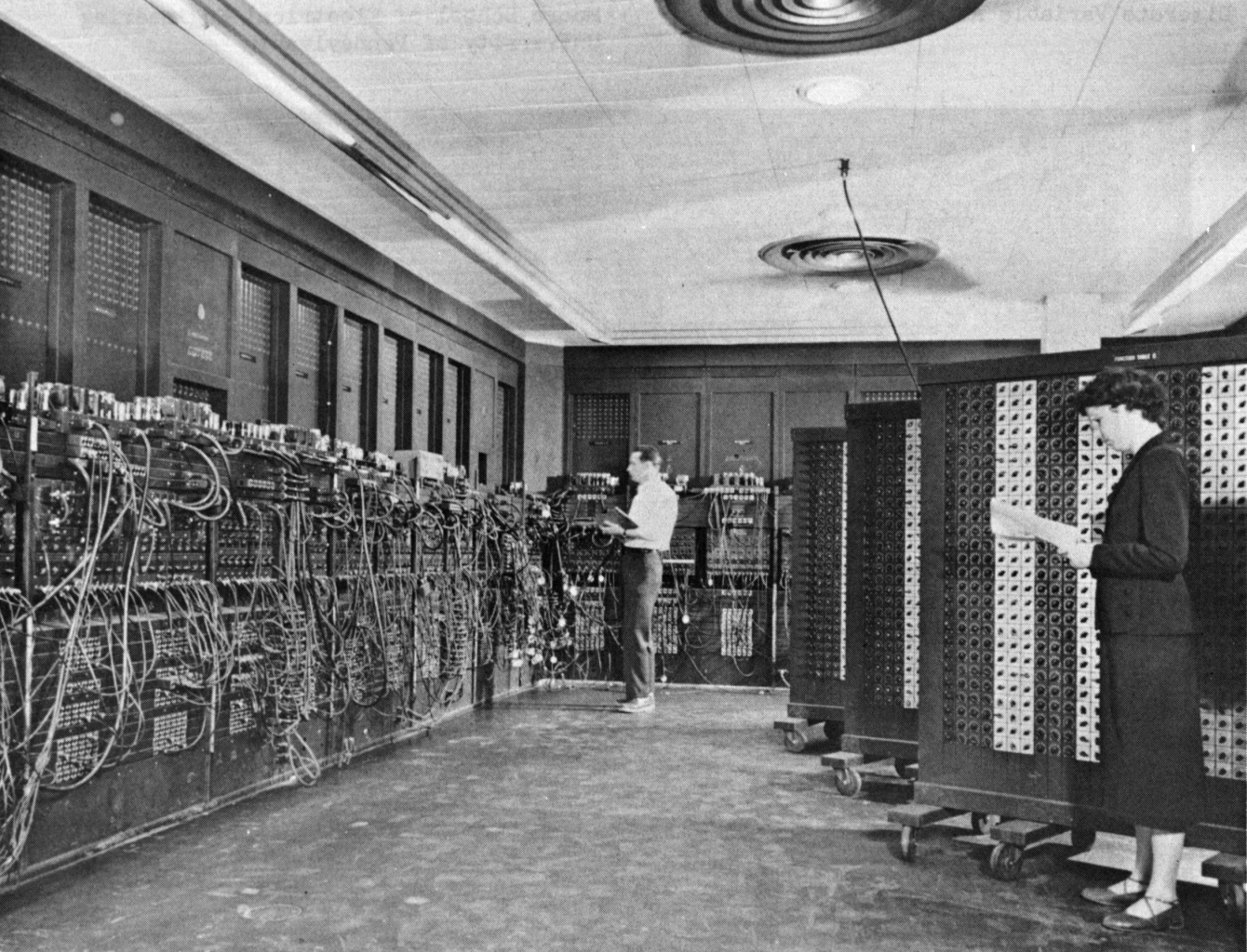 Deux personnes opératrices devant les armoires de l'ENIAC, couvertes de câbles et de panneaux de connexion